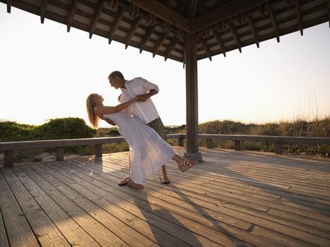 Caucasian couple dancing under gazebo at the beach.