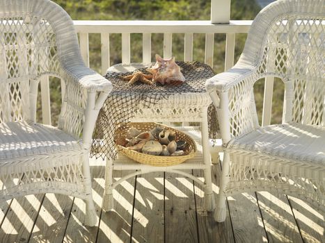 Two wicker chairs with table between them with seashells.