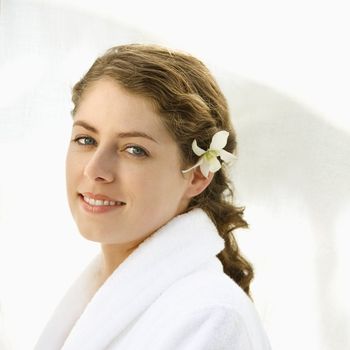 Attractive Caucasian mid-adult woman wearing robe with orchid flower in hair smiling at viewer.