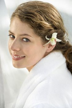 Pretty Caucasian mid-adult woman wearing white terry robe with white orchid flower in hair.