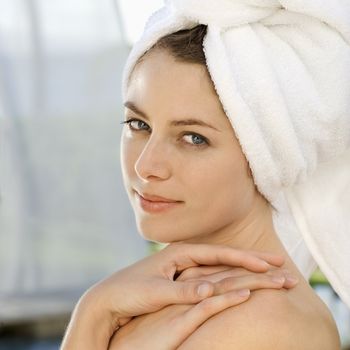 Caucasian mid-adult woman wearing towel around head with hands on shoulder looking at viewer.