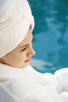 Caucasian mid-adult woman wearing robe and towel on head sitting next to pool.