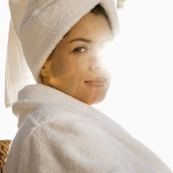 Caucasian mid-adult woman wearing robe and towel on head with sunlight behind her.