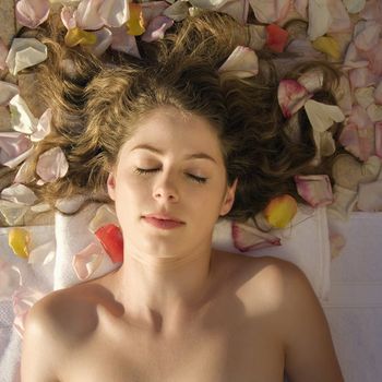 Above view of bare Caucasian mid-adult woman lying down with hair spread out on rose petals.