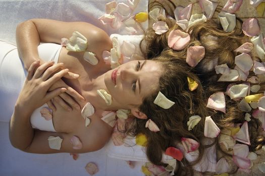 Above view of Caucasian mid-adult woman wrapped in sheet lying down with hair spread out on rose petals.