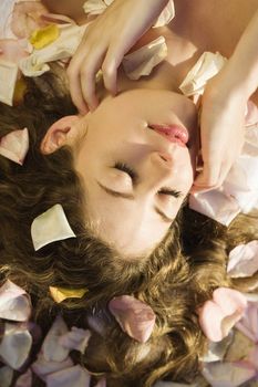 Above view of Caucasian mid-adult woman lying down with hair spread out on rose petals.