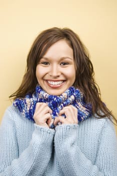 Young adult Caucasian woman wearing sweater holding hands to scarf and smiling at viewer.