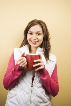 Young adult Caucasian woman holding coffee cup and smiling at viewer.