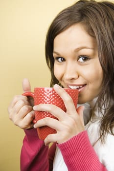 Young adult Caucasian woman holding coffee cup to lips and smiling at viewer.