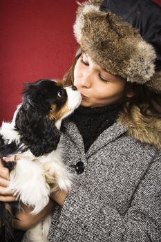 Young adult Caucasian woman wearing fur hat kissing King Charles Spaniel.