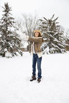 Caucasian young adult female standing throwing a snowball and wearing a straw cowboy hat.