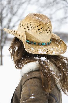 Back view of brunette woman with long hair wearing straw cowboy hat outdoors.
