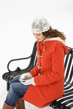 Caucasian young adult female sitting on park bench using PDA.