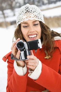 Smiling Caucasian young adult female in winter clothing pointing video camera at viewer.