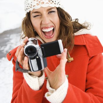 Caucasian young adult female in winter clothing pointing digital camera at viewer and winking.