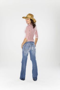 Young Caucasian woman wearing cowboy hat looking over shoulder at viewer and smiling.