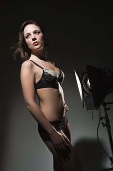 Sexy Caucasian woman in lingerie standing next to spotlight.