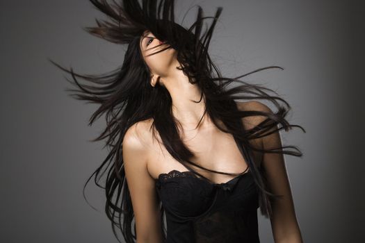 Portrait of pretty young woman flinging long black hair into air.