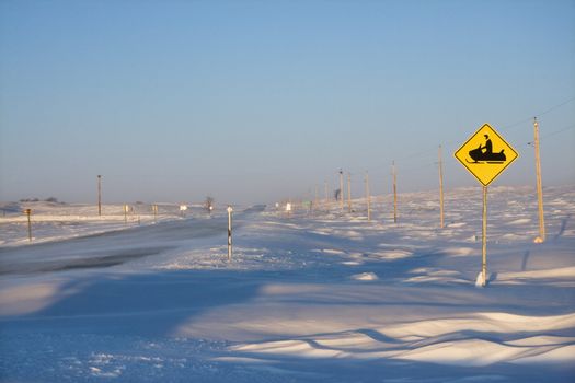 Snow covered road with snowmobile crossing sign.