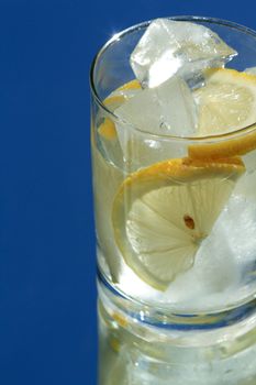 Glass of water with lemon and ice cubes on blue background