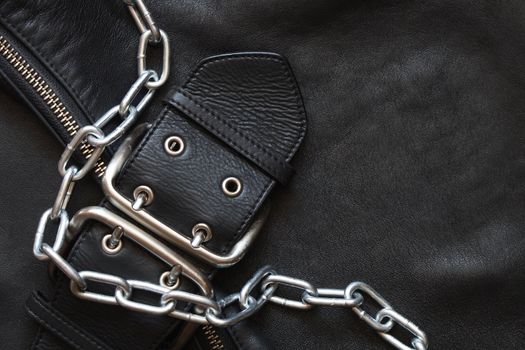 Metal chain lying on black leather background with clasp and zipper