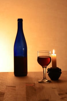 Wineglass near bottle of red wine and candle on nice brown background