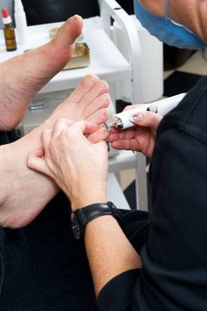 Foot therapist working om adult male feet, fixing the nails and skin. 