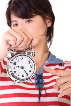 Woman holding alarm clock and pointing, time concept.