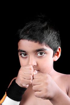 A portrait of an Indian kid in a boxing pose, on black studio background.