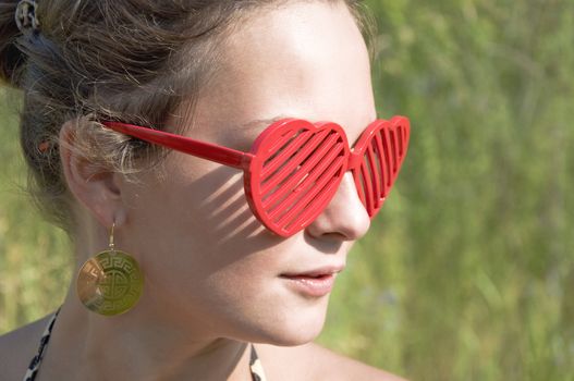 Beautiful young girl in red sunglasses in the form of hearts. Summer portrait, close-up. Outdoor photoset.