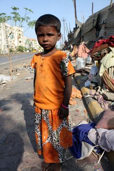 A poor Indian beggar girl anxiously standing by the side of a street.