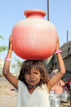 A poor Indian girl carrying water to her home in a red plastic pot, due to scarcity of drinking water to poor people in India.
