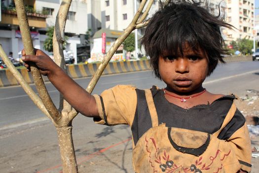 An Indian beggar girl standing under the harsh sun on a streetside.