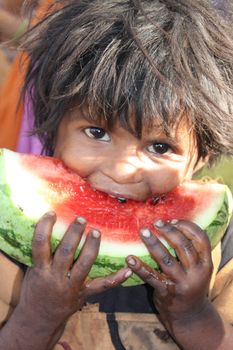 A hungry and sick child from the poor parts of India eating a watermelon.