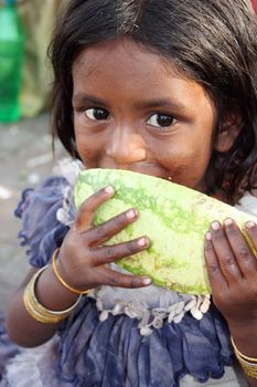 A poor Indian beggar girl hungrily eating a watermelon.
