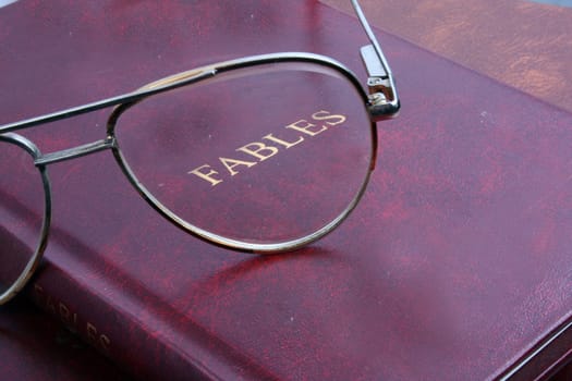 A background with an abstract view of spectacles on a very old book, with the glass focussing on the title - Fables.