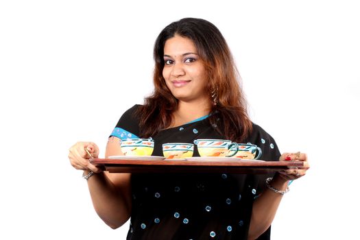 A traditional young Indian woman getting tea in a wooden tray for serving, on white studio background.
