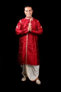 A handsome young Indian guy in a traditional Indian welcome pose, on black studio background.