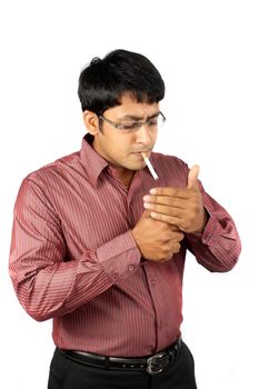 An Indian office executive lighting his cigarette during a break, on white studio background.