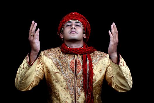 A rich young Afghan man in prayers, on black studio background.