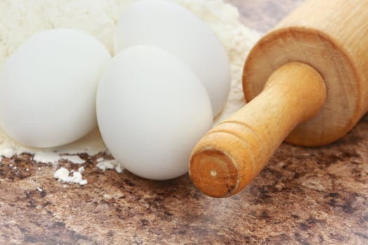 Macro of an old rolling pin, eggs and flour. Extreme shallow DOF with selective focus on tip of rolling pin.