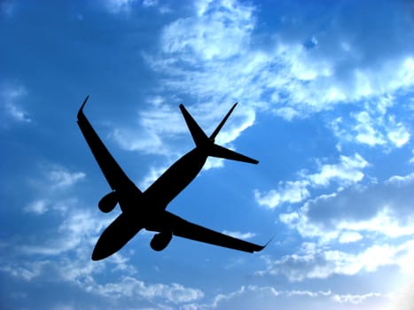 A background with a view of an airplane silhouette against the backdrop of a blue sky with little white clouds.