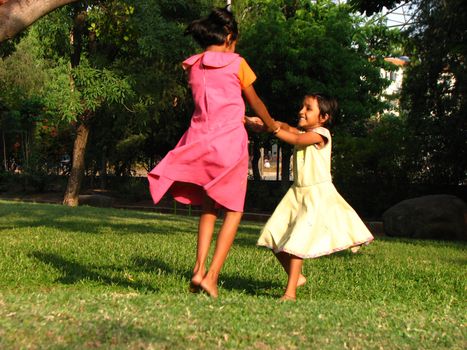 Two poor girls in India playing in a garden going round n' round. Picture in motion.
