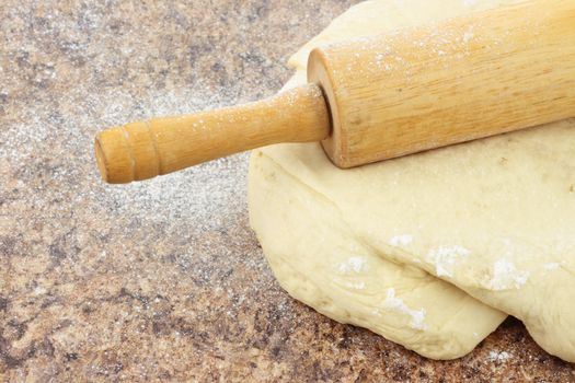 Close up of bread dough being rolled out on a stone counter top. 