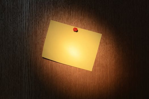 Yellow note pad hanging on dark wooden background under light beam from flashlight