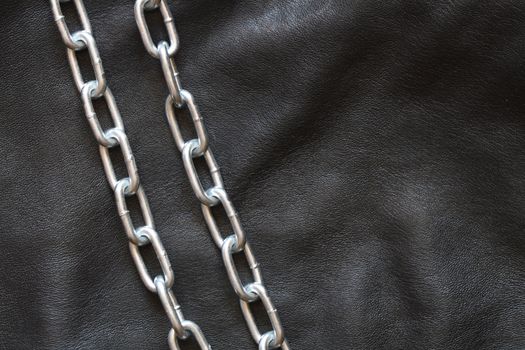 Two metal chains lying on black leather background