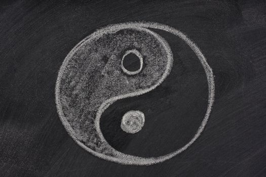 yin and yang symbol sketched with white chalk on a blackboard with eraser smudges