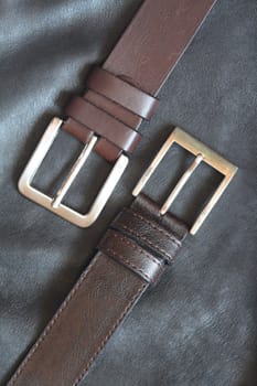 Closeup of two belts lying on black leather background