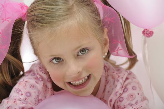 a pretty young blond girl smiling and playing with pink balloons