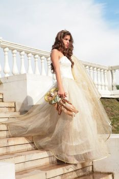 dark-haired princess in white-golden gown with doll goes on step palace